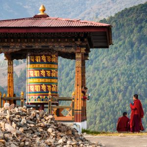 Punakha/Bhutan - March 1, 2016:  young women monks of the Buddhist monastery in their traditional red robes before classes next to the prayer wheel against the background of the Himalayan mountains